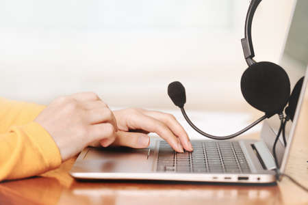 Laptop. headphones or headset on wooden desk and plain background. Female hands over laptop. Distant...