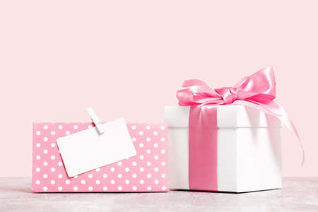 White gift box with shining pink ribbon bow on pink background with mockup gitf card. Gift or...