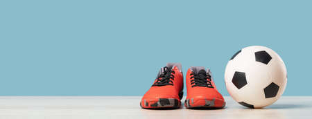 Soccer ball with orange cleats against blue background, front view with copy space, football or sports class and tournament at school concept. Long bannerの写真素材