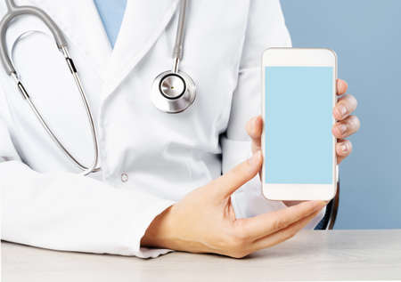 Cropped view of female doctor holding a smartphone with an medical app. Blank blue mockup copy space...