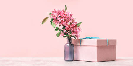 Pink pastel holiday banner with gift box and spring or summer flowers branch in a vase. Monochrome.,...