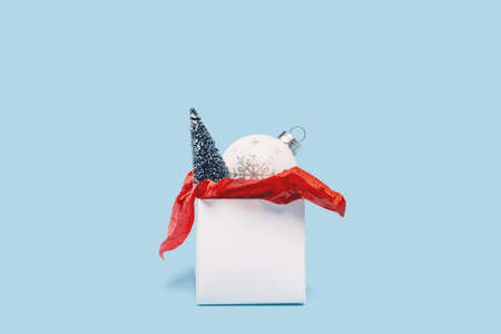 One red and white gift box and ornaments with Christmas tree on baby blue background. Minimal centered. Merry Christmas and Happy New Year gift shopping and sale conceptの写真素材