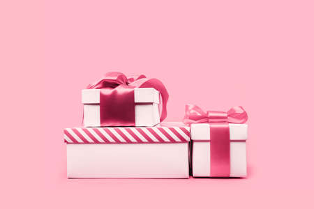 three assorted white gift boxes with shining pink ribbon bow on pink background. Gift or holiday concept. Mothers Day, birthday wedding or St Valentines day banner with copy spaceの写真素材