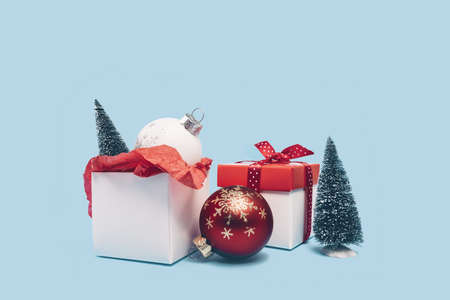 Two red and white gift boxes and ornaments with Christmas trees on baby blue background. Assorted...