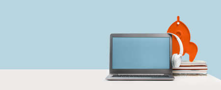 Side view of slim laptop with headphones headset on white desk. Mockup screen. Rocket lamp on books. Distant learning. working from home, online courses or support. Audio podcast. Achievement bannerの写真素材