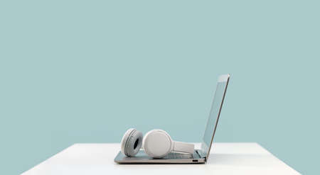 Laptop. Mockup screen and wireless headphones on white desk. plain blue background. Distant learning. working from home, online courses. minimal. Helpdesk support or call center headsetの写真素材