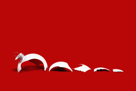 White broken glass bauble on red Christmas background. Winter holiday season depression and stress,...