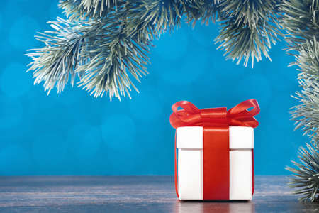 Christmas ornaments. White gift box with red ribbon under Christmas tree. Happy new year greeting...