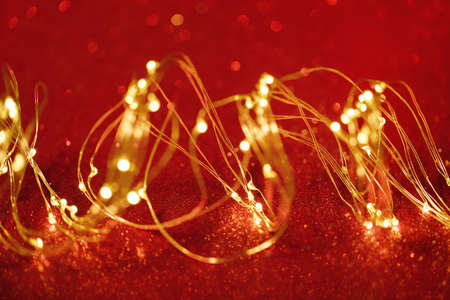 christmas background. Twisted golden xmas lights wire on sparkly festive red background. Copy space. Merry Christmas or Happy New Year cardの写真素材