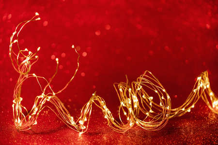 christmas background. Twisted golden xmas lights wire on sparkly festive red background. Copy space. Merry Christmas or Happy New Year cardの写真素材