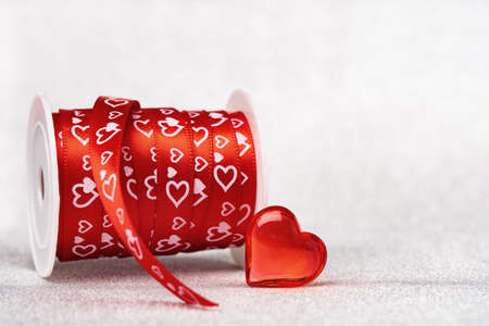 A roll of red gift ribbon with hearts for St Valentines day or 14 February. Glass heart. Minimal wide banner with copy spaceの写真素材