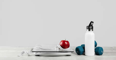 Red apple, white tape measure around a water bottle dumbbells with glass bathroom scale on gray. Front view copy space. Healthy lifestyle, weight losing management and hydration concept bannerの写真素材