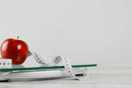 Health. white tape measure oand red apple n top of glass bathroom weighing scale on gray. Front view copy space. Healthy lifestyle, weight losing management and hydration conceptの写真素材