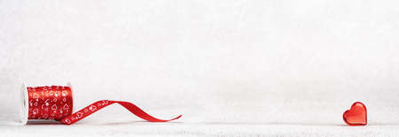 A roll of red gift ribbon with hearts for St Valentines day or 14 February. Glass heart. Minimal wide banner with copy spaceの写真素材