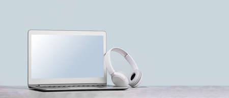 Laptop with wireless headphones on white deskの写真素材