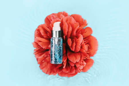 Cosmetics spa serum bottle on water waves and red flowerの写真素材