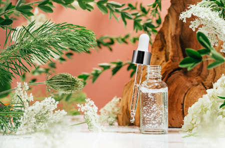 Cosmetic amber glass dropper bottle in fresh nature setup. Green leaves white flowers on pink....