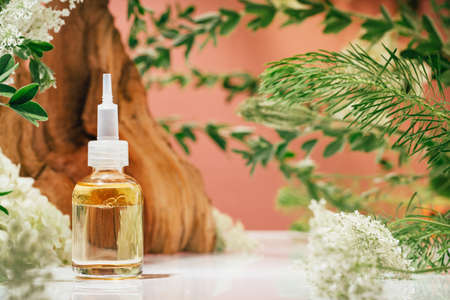 Cosmetic amber glass dropper bottle in fresh nature setup. Green leaves white flowers on pink. Essential aroma oil or face care serum essence. natural beauty and cosmetics. Pink forestの写真素材