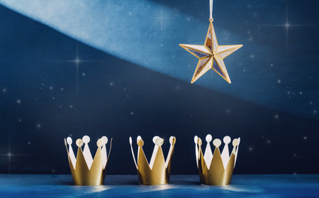 three shiny golden paper crowns and a star in the blue sky. Epiphany and three kings day holiday...