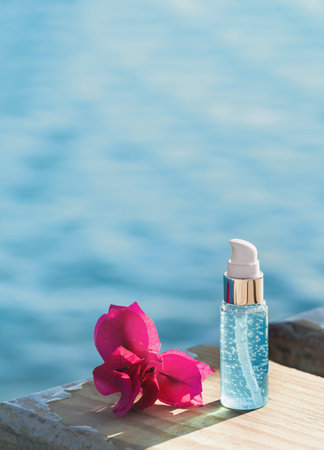 Natural beauty essence concept mockup bottle on seaside deck with red flower. Face and body spa serum care fresh concept. Hydration and moisturizer. Holiday cosmeticsの写真素材
