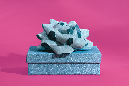 Blue sparkling gift box with ribbon bow on magenta pink background. Gift or holiday concept. Mothers Day, Fathers birthday wedding or St Valentines day with copy space. Minimal bannerの写真素材