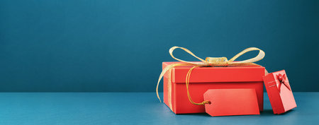 Big and small red gift boxes on blue background. Golden bow and mockup gift tag. Holiday shopping...