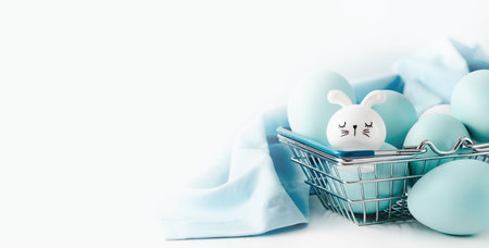 Several blue dyed Easter eggs with cute bunny in metal basket on white table. Easter holiday eggs...