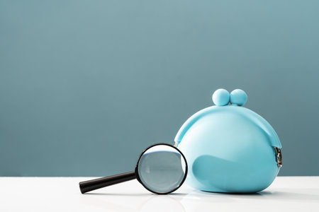 Blue coins purse under magnifying glass on desk. Household budget wages or payment of bills. Find loan or bank. Value for money search conceptの写真素材