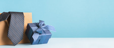 Happy Fathers Day background banner. Side view of blue gift box and brown paper bag, necktie on pastel blue table.の写真素材