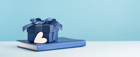 Small luxury gift box with blue bow agenda and white heart. Side view. Fathers day or Valentines day gift for him. Corporate thank you concept or birthday party. Festive sale copy space bannerの写真素材