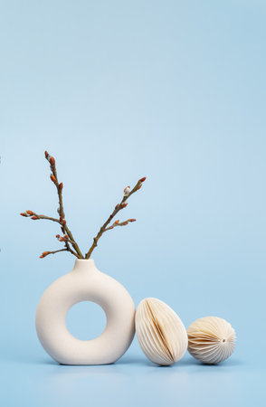 Easter concept. Ivory vase with willow branch and two paper craft Easter eggs on blue background monochromeの写真素材
