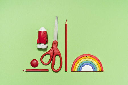Rainbow tag with red stationery. rocket and scissors pencils on green background. copy space for...