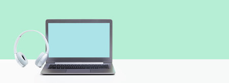 Laptop. Mockup screen and headphones on white desk and plain green background banner. Distant learning. working from home, online courses or support minimal concept. call center headsetの写真素材