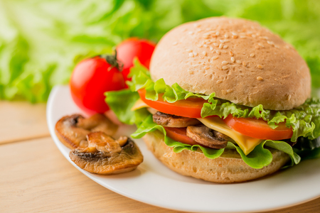 Vegetarian burger with mushrooms and fresh salad on the white plate on wooden table, close upの写真素材