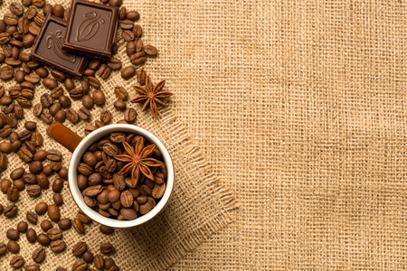 Coffee cup and coffee beans, chocolate, anise on brown burlap. Top view.の写真素材