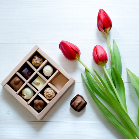 Chocolate candies in the box. Candy box and red tulips for the romantic gift on white background, copy spaceの写真素材