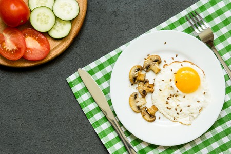 breakfast with fried eggs, mushrooms and vegetables in a white plate on dark background, top view, copy spaceの写真素材