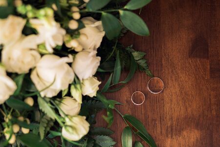 Golden wedding rings on a wooden background with bouquet of flowers, top view, wedding day, loveの写真素材