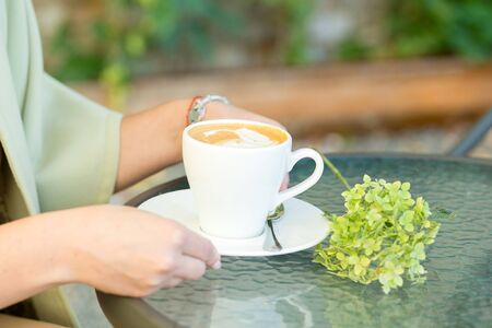 Female hands holding cup of capucchino at the cafe, close upの写真素材