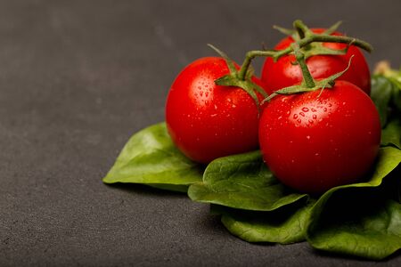 Tomatoes and spinach leaves on black table, close-up, copy space