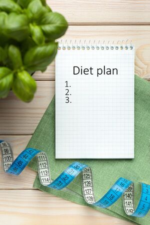 Notepad with diet plan, diet concept, tape measure on wooden background, top view.の写真素材