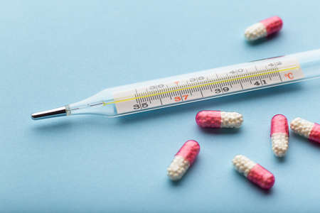 Mercury thermometer with capsule pills on blue background close up, thermometer temperature medical...