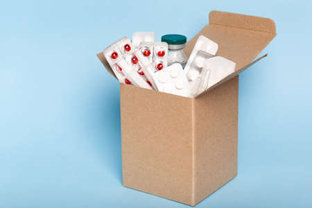 Delivery of medicines home from the pharmacy. Cardboard box with medicines, pills, bottles, injections isolated on blue background.の写真素材
