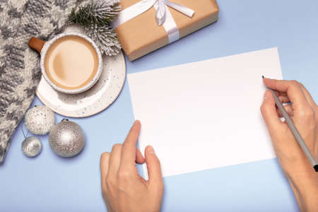 Female hands writing christmas card, paper gift box and coffee on blue background, goals conceptの写真素材