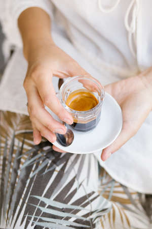 Espresso in glass cup in female hands close up. Coffee break concept.の写真素材