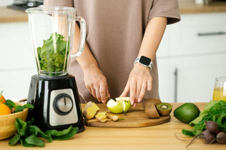 Woman cooking breakfast from green fresh smoothie at the kitchen, close up. Preparing natural detox lemonade at table in kitchenの写真素材
