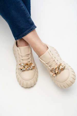 Modern female sneakers. Beige faemale shoes on feet. Sneakers closeup om whiteの写真素材
