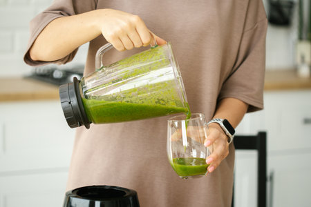 Female hands pour green smoothie into a glass close up. Healthy food, breakfast. Healthy lifestyle,...