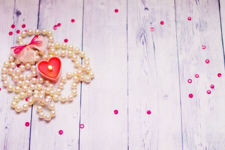 on a white wooden background red candle pearl beads romantic backgroundの写真素材