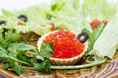 red caviar in a tartlet on a plate with greens and olives close up on a white backgroundの写真素材